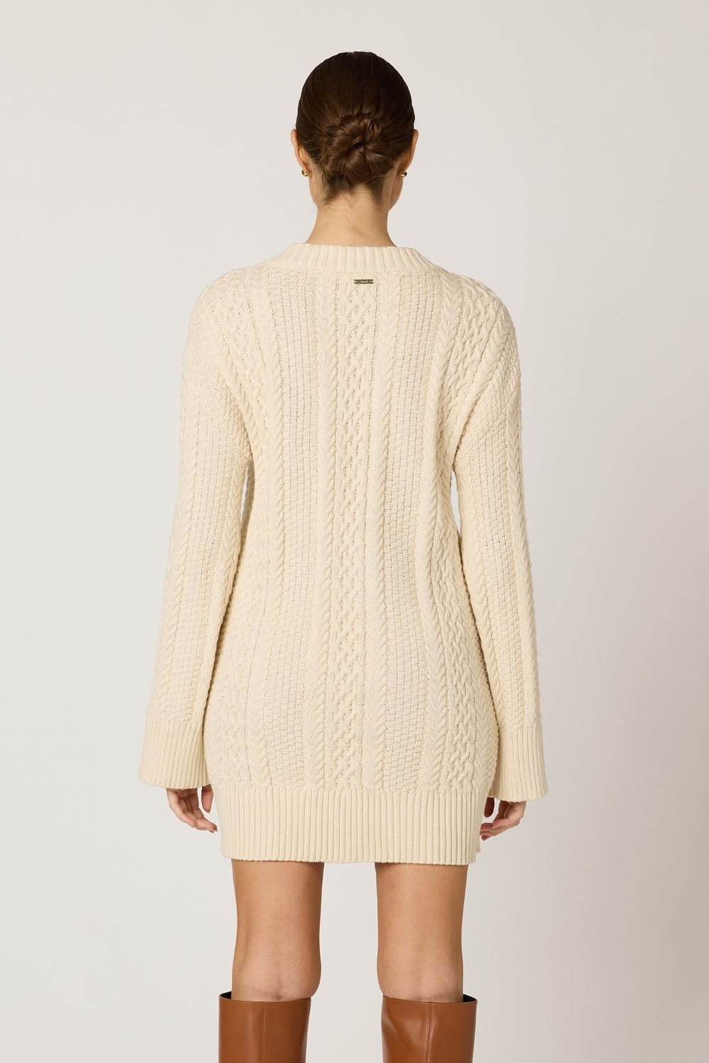 Woman wearing a cream cable knit cardigan on a plain background