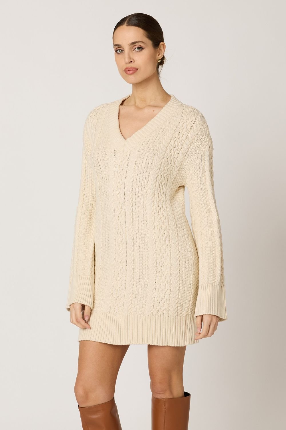 Woman wearing a cream cable knit sweater dress on a plain background