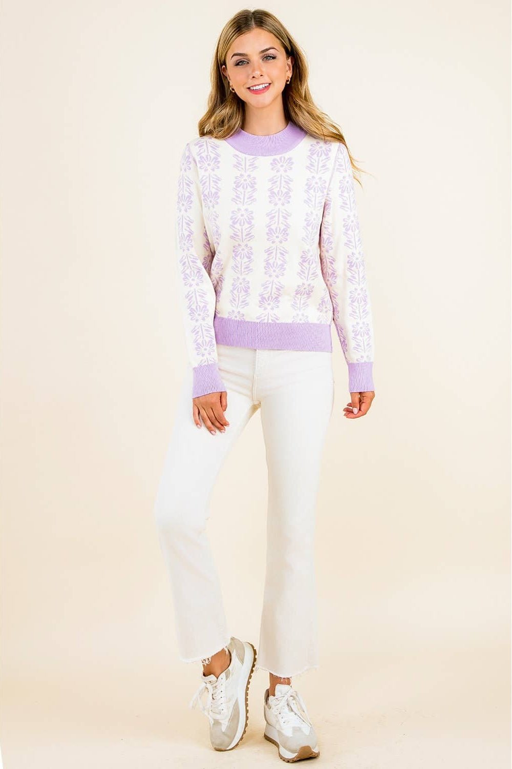 Woman wearing a light purple sweater and white pants on a beige background