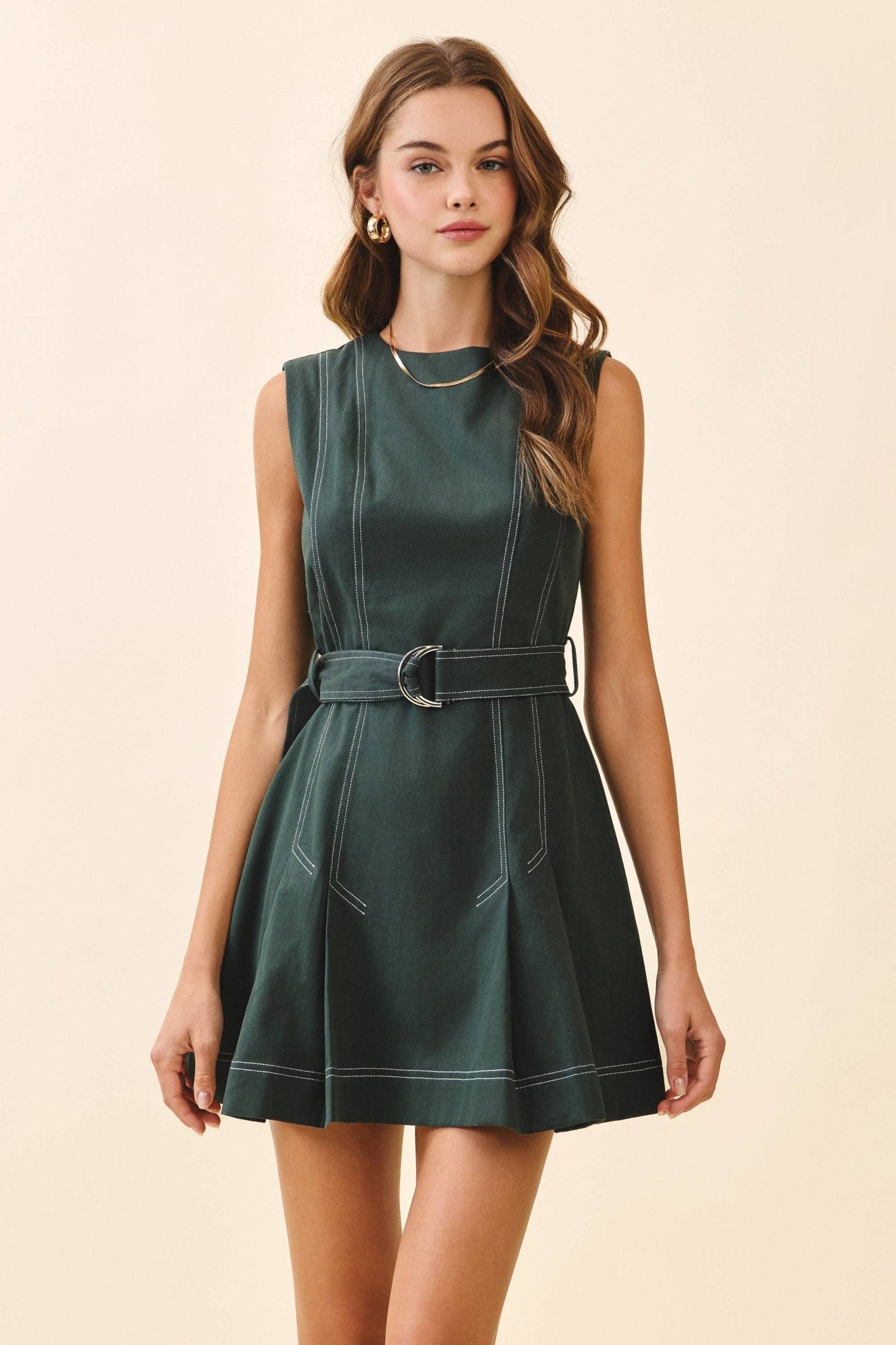 Woman wearing a green dress with a belt on a beige background