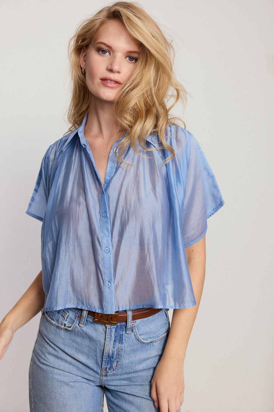 Woman wearing a light blue sheer blouse and jeans on a plain background