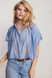 Woman wearing a light blue sheer blouse and jeans on a plain background